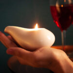 Massage candle jar held in the hand with two wine glasses in the background