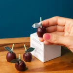 Cute maroon cherry candles kept on the box of candles. It is very small set of candles. A woman holding one cherry candle that is a very realistic candle