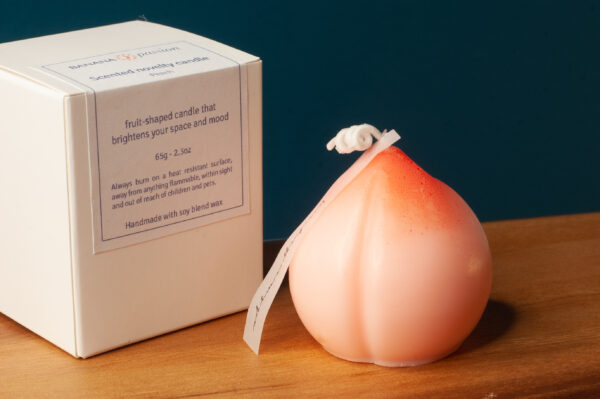 Peach shaped novelty candle next to a beautiful white packaging box