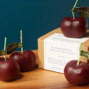 4 novelty cherry candles along with the kraft packaging box on a wooden table