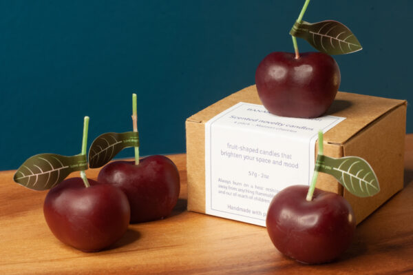 4 novelty cherry candles along with the kraft packaging box on a wooden table