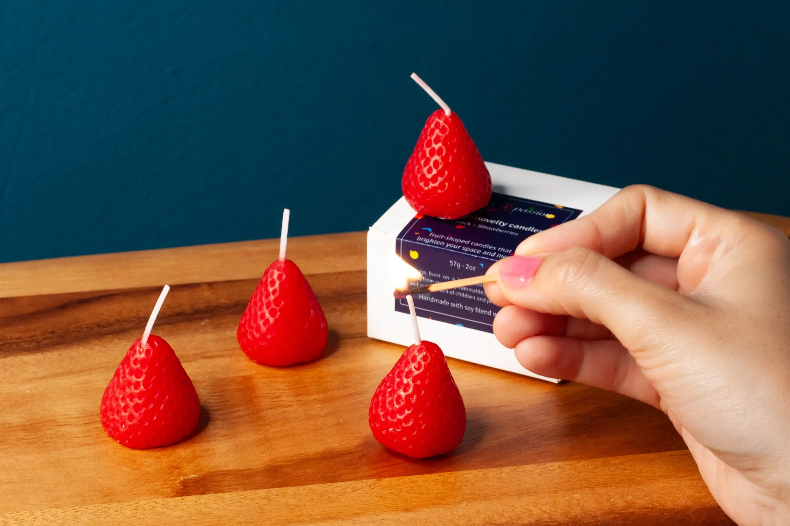Strawberry shaped candles being lit by a woman. These strawberry candles look like a strawberry and smell like a strawberry fruit.
