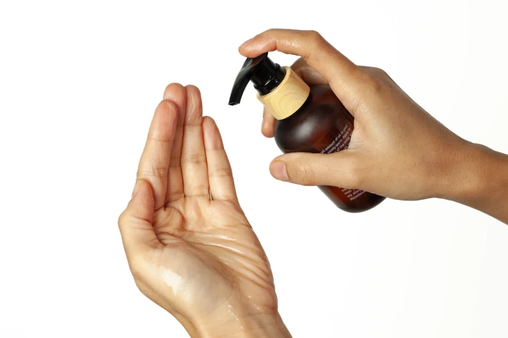 Massage oil being sprayed on another hand of a woman.