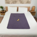 Heather Grey Waterproof Sex blanket on the bed with a banana on top it for scale. There is a painting on the wall and there are two floating bed side tables.