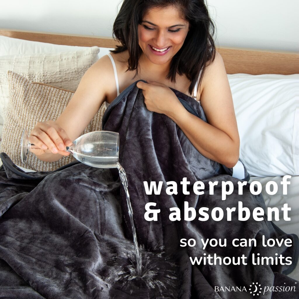 Dark grey waterproof blanket with water being poured onto the surface to show it stays dry underneath.