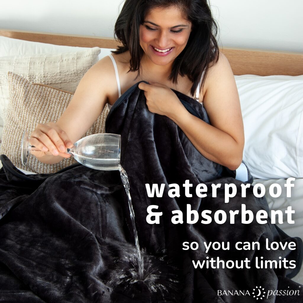 Woman pouring water from a glass onto a velvety waterproof blanket spread on a bed, showing how the soft intimacy blanket absorbs liquid while keeping the sheets underneath dry.