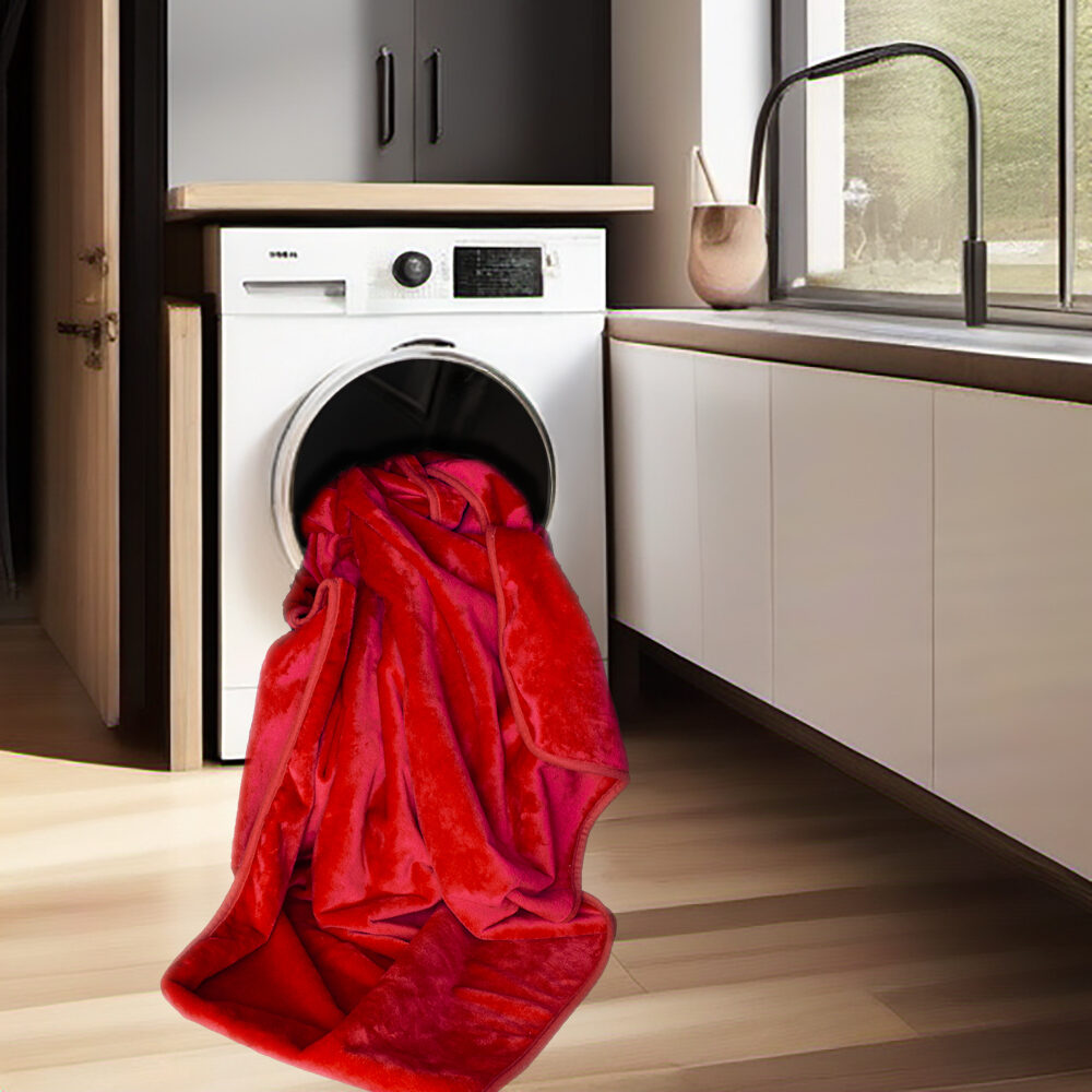 Red velvety waterproof blanket seen sticking out of a laundry machine, ready to go for washing.
