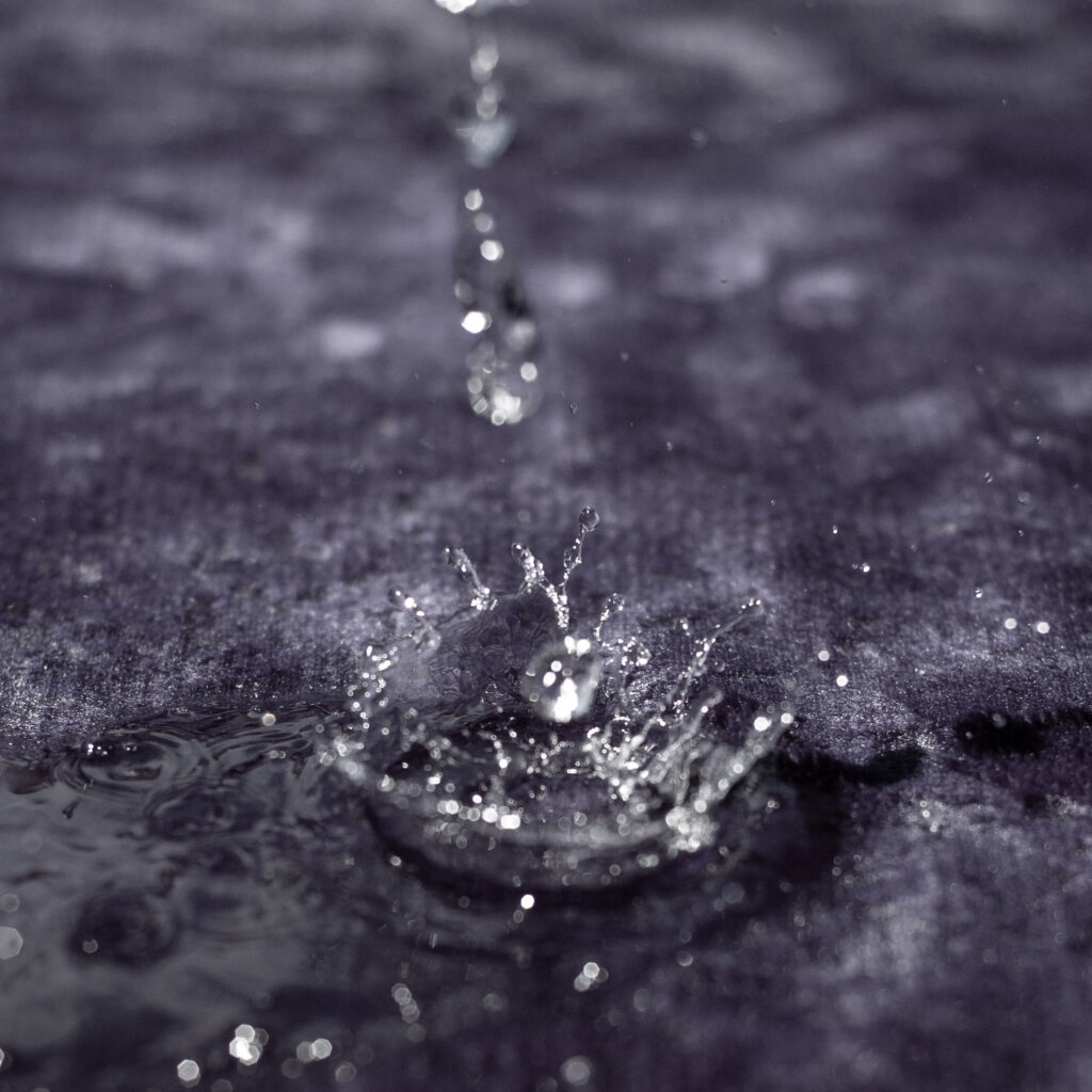 Droplets of water fall onto a waterproof blanket, creating a clear splash on the blanket.