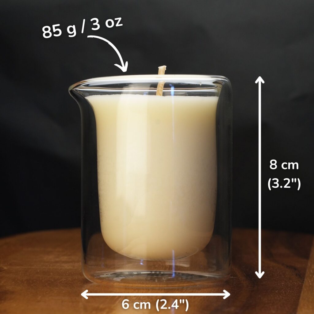 Size of a double glass jar massage candle shared which is 85gm in weight. 85g candle jar beside a hand for scale, 6cm wide and 8cm tall