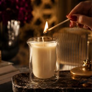 Banana Passion massage candle burning in a double-walled glass jar on a bedside table